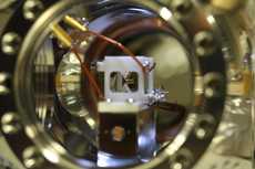 A small white device is connected to two wires in a metal chamber. It is visible through a circular port hole.