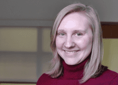 a woman smiling at the camera and wearing a red turtleneck